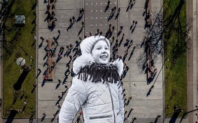 2022年、アーティストJR氏が制作した5歳のウクライナ人少女ヴァレリーアちゃんの巨大な画像が、ポーランドとの国境から7キロ離れたウクライナ領内でボランティアの手によって広げられたところ。ヴァレリーアちゃんは、ウクライナのゼレンスキー大統領の生まれ故郷クルィヴィーイ・リーフの出身。（PHOTOGRAPH BY JR, REDUX）