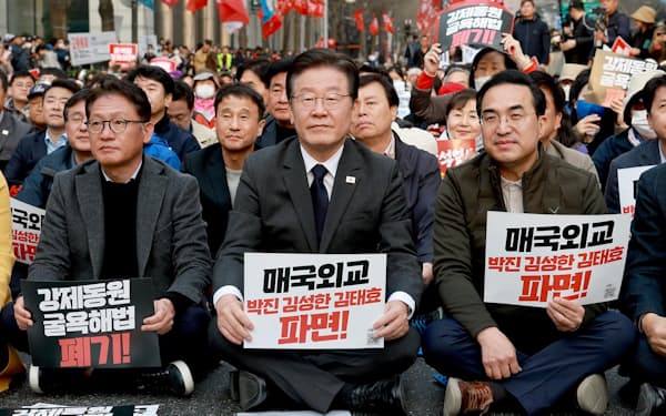 野党「共に民主党」の李在明代表（中央）は「売国外交」のプラカードを掲げて尹政権を批判する（3月25日、ソウル）