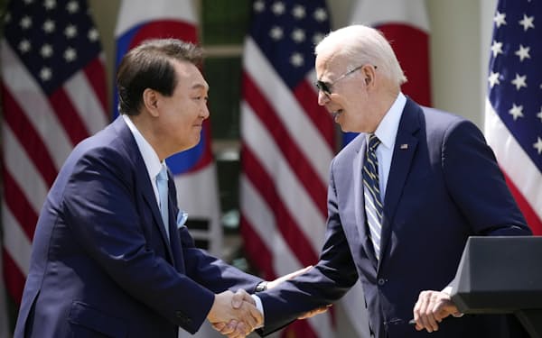 26日、米ホワイトハウスで共同記者会見をし、握手を交わすバイデン大統領（右）と韓国の尹錫悦大統領＝AP・共同