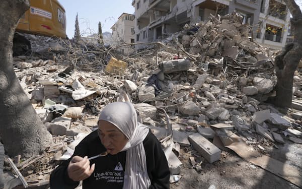 5日、地震で大きな被害が出たトルコ南部ハタイ県アンタキヤで、崩れた自宅の前で食事をとる女性＝共同