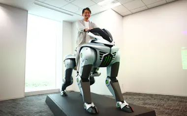 報道向け説明会で川崎重工業の4脚ロボット「CORLEO(コルレオ)」にまたがる天辰祐介総括部長(28日、東京都大田区)