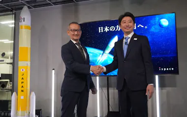 三菱重工業の五十嵐巌・宇宙事業部長㊧とispaceの袴田武史CEO、左はH3ロケットの模型(29日、東京都中央区)