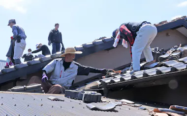 強い日差しの中、屋根に上がり割れた瓦を撤去する住民の友人ら(1日午前、熊本県宇城市)