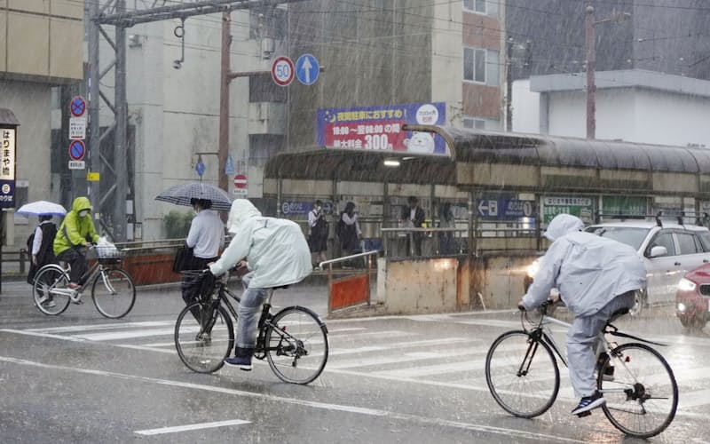 強い雨の中、自転車で横断歩道を渡る人たち（2日午前、高知市）=共同