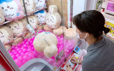 クレーンゲームで漫画のキャラクターのクッションを狙う女性(大阪市中央区のタイトーステーション難波店)