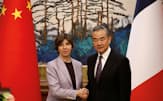 握手する中国の王毅外相とフランスのコロナ外相（24日、北京）=ロイター