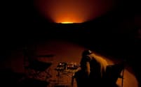 トルクメニスタンの砂漠で何十年も燃え続ける巨大なメタンガス噴出孔ダルバザ・クレーターの近くにテーブルセットを置いたツアーガイド。（PHOTOGRAPH BY CAROLYN DRAKE, MAGNUM PHOTOS）