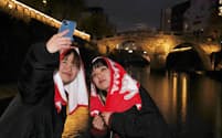 ライトアップされた観光名所「眼鏡橋」で自撮りする観光客（12月上旬、長崎市）