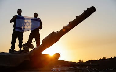 11月29日、ハマスとの一時休戦中にガザとの国境付近で自国の国旗を掲げるイスラエル兵=ロイター