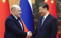 ロシアのミシュスチン首相㊧と握手する中国の習近平国家主席（20日、北京）＝タス・共同