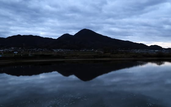 早朝の淡い光に浮かぶ二上山の山容。雄岳（中央右）と雌岳（同左）が池に映る（奈良県香芝市より望む）