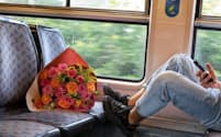 フランスのパリとトゥルナン・アン・ブリー間を走る列車の車内で、花束を置いて携帯電話をチェックする若者。2023年のピュー・リサーチセンターの報告書によれば、30歳未満の調査参加者の53％が「恋人を見つけるのにデートアプリを使用した経験がある」と答えている。（PHOTOGRAPH BY SOPHIE CHIVET, AGENCE VU/REDUX）