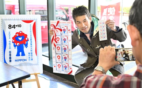 販売開始となった大阪・関西万博の記念切手を購入し、撮影する男性（12日午前、大阪市北区）