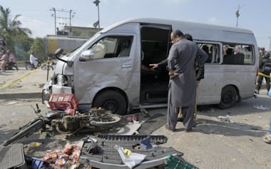 19日、自爆テロの現場で、損壊した車を調べる担当者ら（パキスタン南部カラチ）=AP