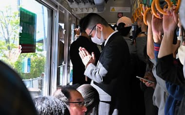 脱線事故の現場付近を走行する電車内で手を合わせる乗客（25日午前、兵庫県尼崎市）=代表撮影