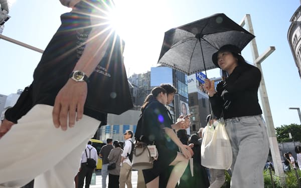 強い日差しのもと、日傘を差して歩く人ら（5日、東京都中央区）