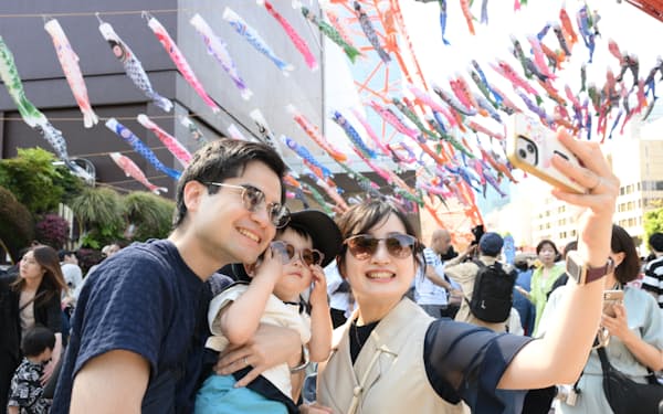こいのぼりが掲げられた東京タワーで、強い日差しのもとサングラス姿で写真に納まる親子連れ（5日、東京都港区）=釜江紗英撮影