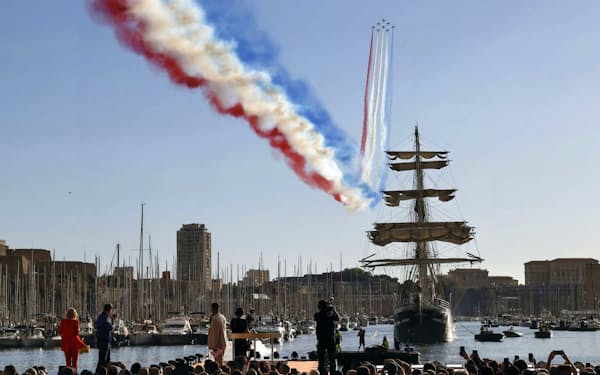 フランス南部マルセイユの旧港に到着した聖火をのせた帆船。その上空を空軍機がカラースモークで彩った（8日）=共同