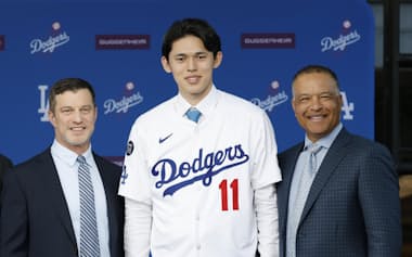 ドジャースの入団記者会で佐々木朗希はロバーツ監督(右)からユニホームを着せられた=共同