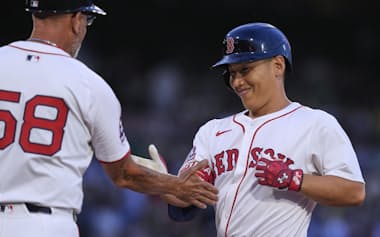 復帰戦の第1打席で安打を放ち、笑顔で一塁ベースコーチとタッチを交わす吉田(9日)=AP