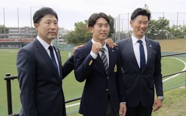 西武からドラフト1位で指名され、写真に納まる明大の小島㊥。右は西武の広池浩司球団本部長(31日、東京都府中市)=共同