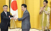 ジャパンSDGsアワード表彰式で本部長賞を受けた北海道下川町の谷町長（左）にトロフィーを手渡す安倍首相。右は推進大使のピコ太郎さん