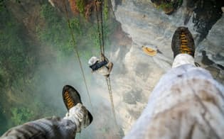 宙吊りになった写真家レナン・オズターク氏の足。ハチに刺されないようテープを巻いている。その下で縄ばしごを登るのはクルン族最後の蜂蜜採りマウリさん（PHOTOGRAPH BY RENAN OZTURK）