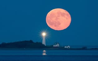 2017年7月10日、米国のボストン灯台の背後からのぼった満月。表面は金色に輝いている（PHOTOGRAPH BY BABAK TAFRESHI）
