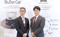 ローランド・ベルガーの長島聡社長（左）と慶応義塾大学の田中浩也・教授（右）。ローランド・ベルガーが東京モーターショーで展示した「バトラーカー」のポスターを背景に撮影