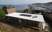 ハウステンボス・スマートハウスのデザインは、ハーバーへ向かう軸線を建物内部に取り込み、テラスによって住居を2分。回遊性のあるプラニングとした。屋根には太陽光発電パネルと太陽熱温水パネルが載っている。撮影日は5月20日（写真:日経アーキテクチュア、以下同じ）