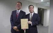 認定書を報道陣に見せるKDDIの田中孝司社長（左）とUQコミュニケーションズの野坂章雄社長（右）