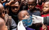 ケニア、ナイロビの恵まれない家族に食事を配る援助隊員が、男の子の顔にマスクを当ててみせる。新型コロナウイルスのパンデミックが経済危機を引き起こし、世界中の低所得層にしわ寄せが及んでいる（PHOTOGRAPH BY FREDRIK LERNERYD, AFP/GETTY）