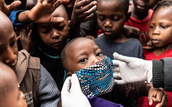 ケニア、ナイロビの恵まれない家族に食事を配る援助隊員が、男の子の顔にマスクを当ててみせる。新型コロナウイルスのパンデミックが経済危機を引き起こし、世界中の低所得層にしわ寄せが及んでいる（PHOTOGRAPH BY FREDRIK LERNERYD, AFP/GETTY）