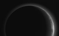 冥王星の山々や氷の平原や谷が日没の光にほのかに輝き、かすんだ空も光を放っている。（PHOTOGRAPH BY NASA/JHUAPL/SWRI）
