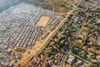 青い芝生とプールが見える住宅街から道路を隔てて、トタンの小屋が立ち並ぶ地区が広がる。南アフリカ、ヨハネスブルク郊外のブルーボスランド(PHOTOGRAPH BY JOHNNY MILLER) 青い芝生とプールが見える住宅街から道路を隔てて、トタンの小屋が立ち並ぶ地区が広がる。南アフリカ、ヨハネスブルク郊外のブルーボスランド(PHOTOGRAPH BY JOHNNY MILLER)